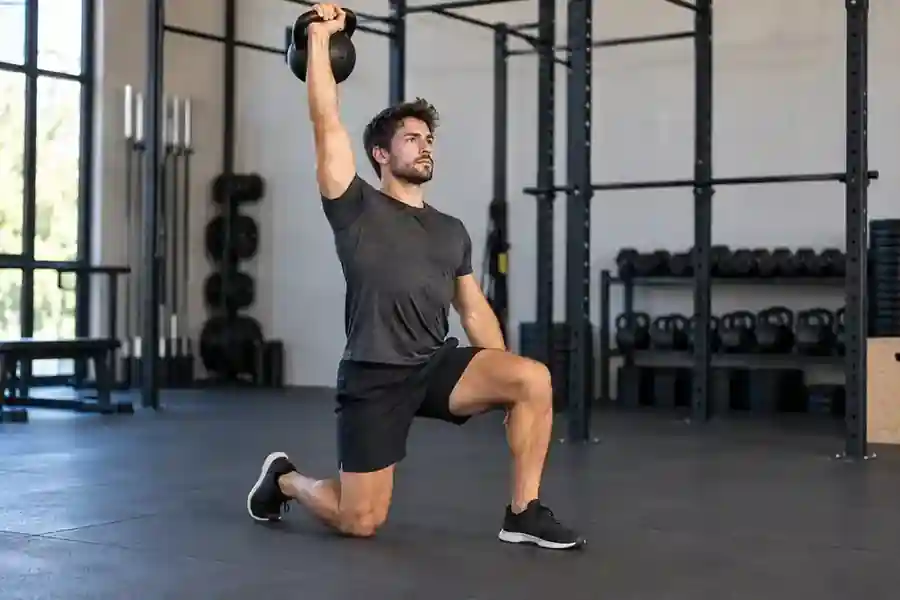 Persona realizando press con kettlebell desde media rodilla